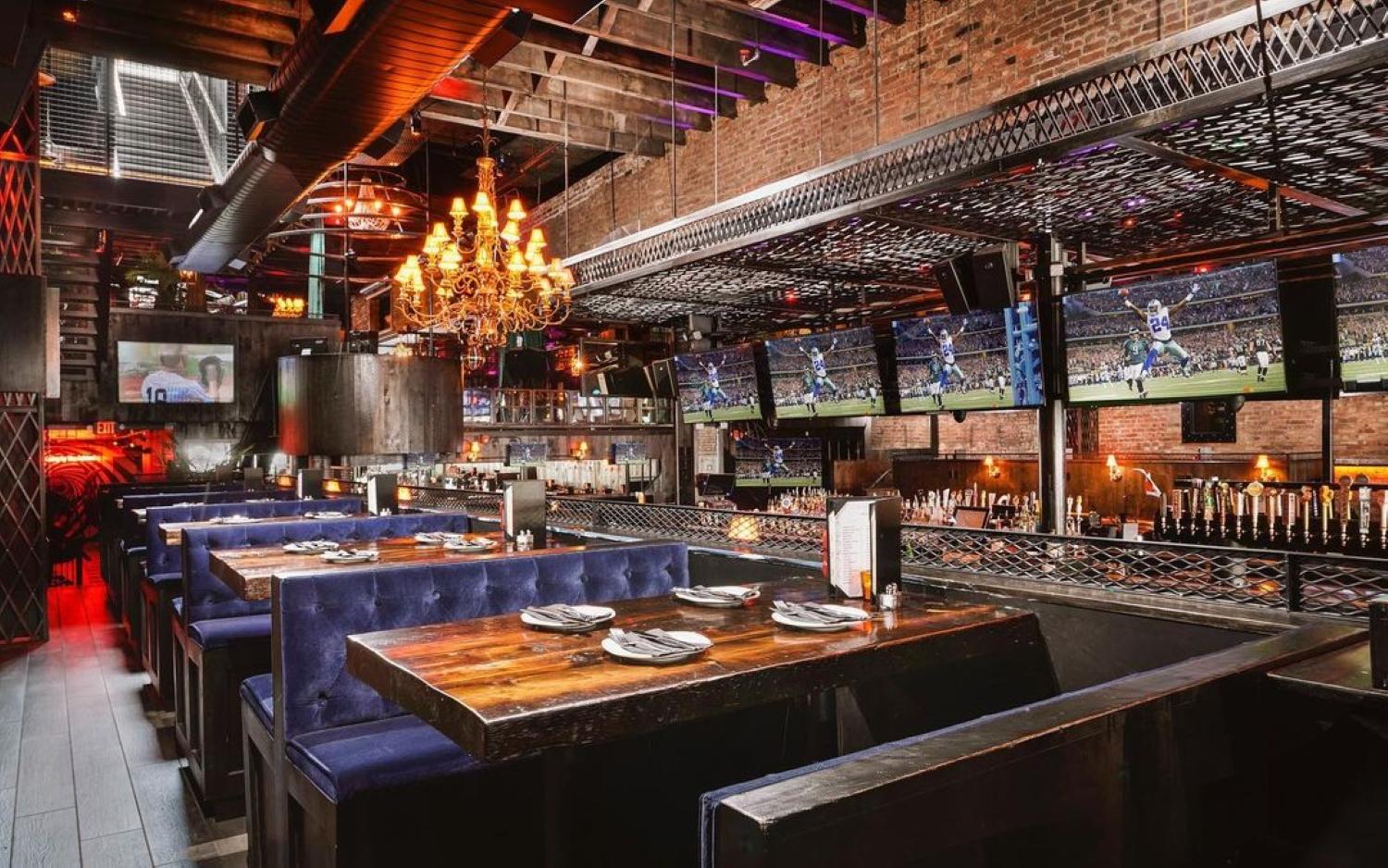 A dining room with exposed brick walls, chandeliers, and blue velvet banquettes at The Ashford.