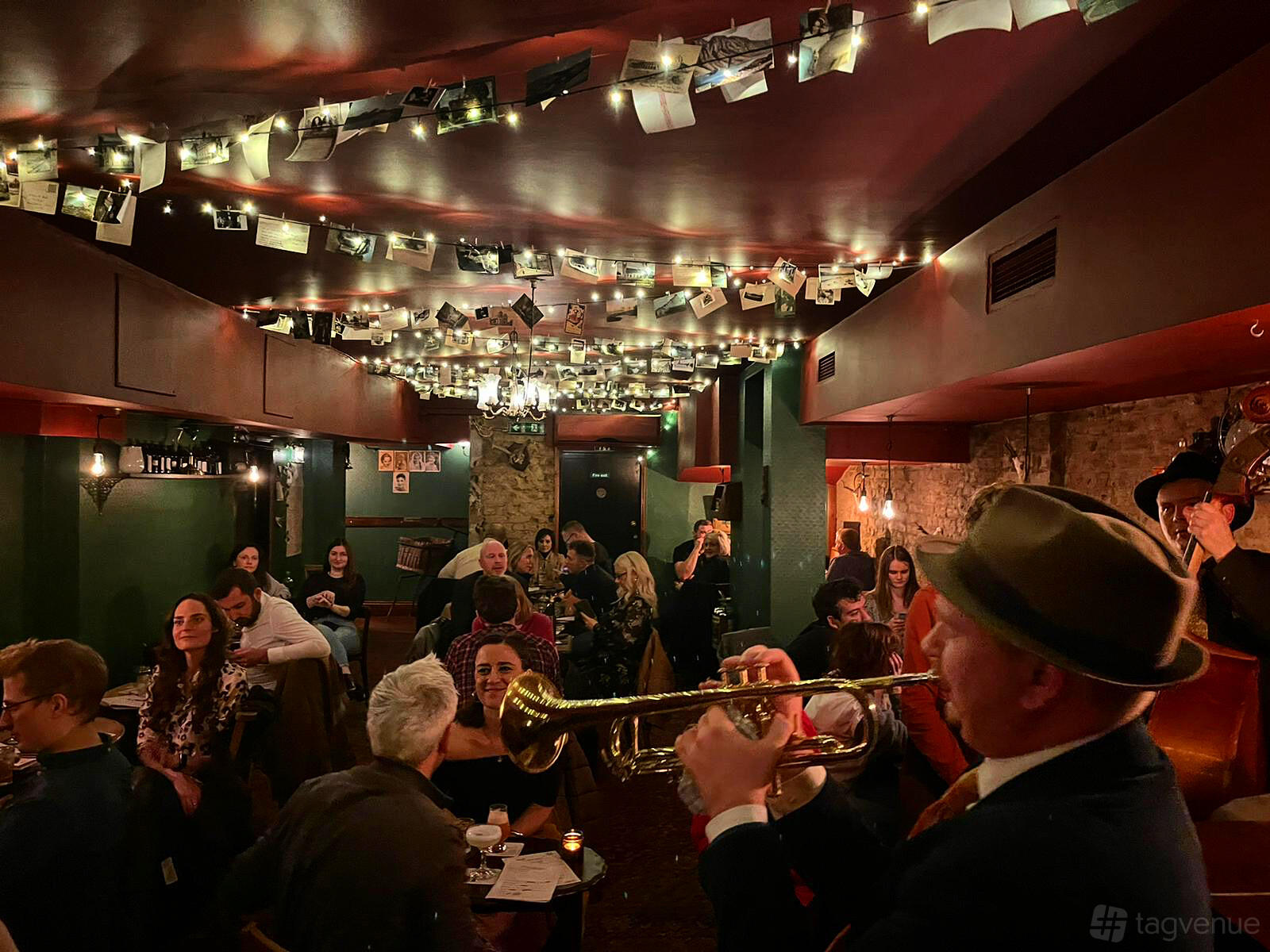 A cocktail bar with exposed brick walls, low lighting, and ceiling decorations featuring photos at Evans & Peel Detective Agency.