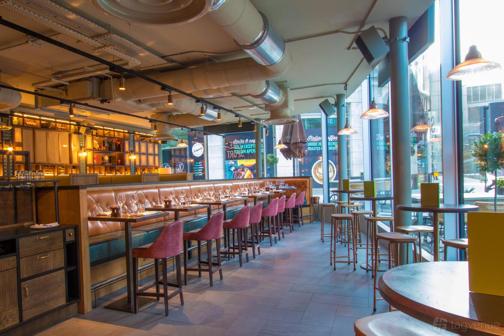 A bar in a pub with tan leather banquette seating, high tables, and floor-to-ceiling windows at Broadwood.