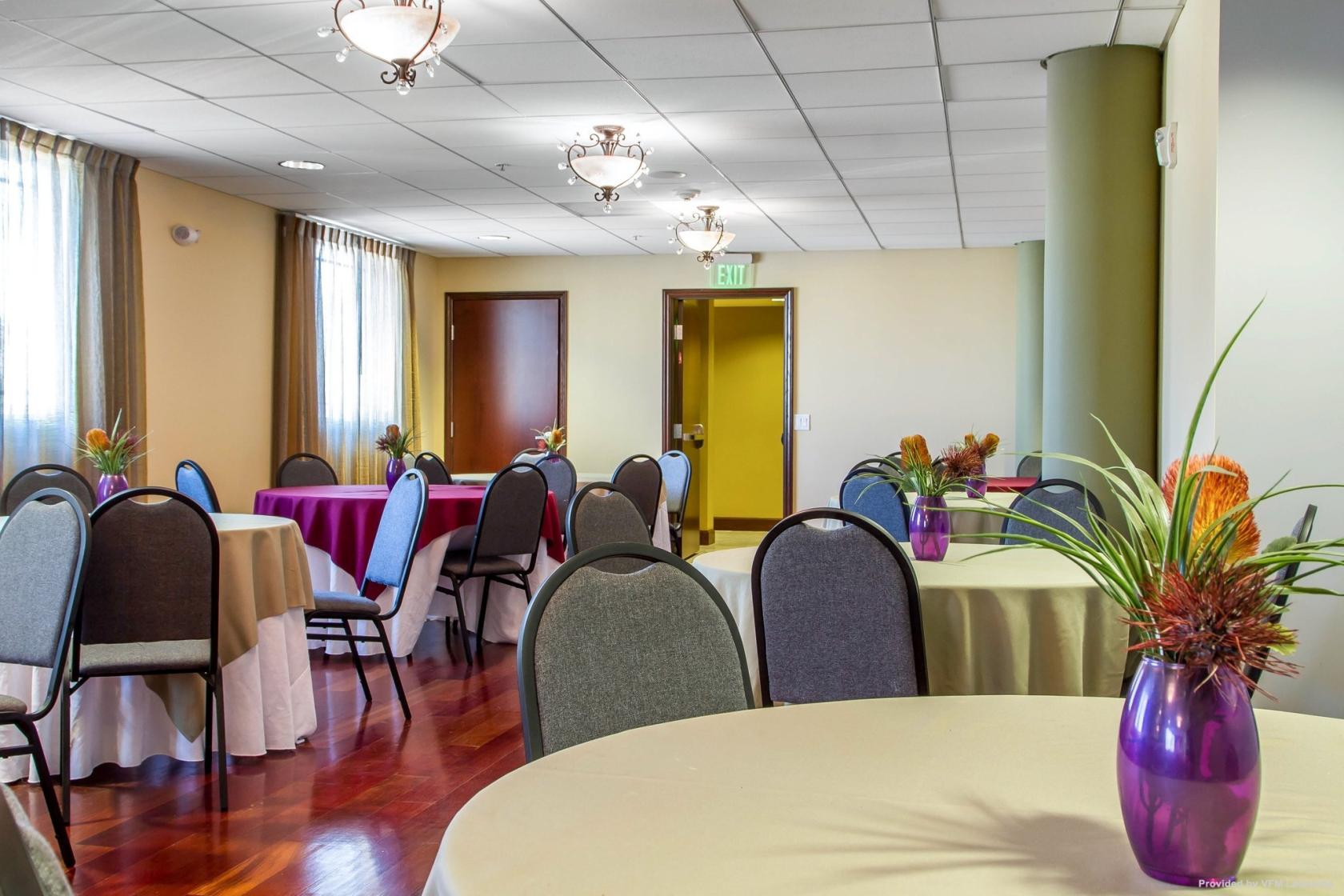A hotel meeting space with round tables, beige linens, and purple floral centerpieces at Villa Montes Hotel, Ascend Hotel Collection.