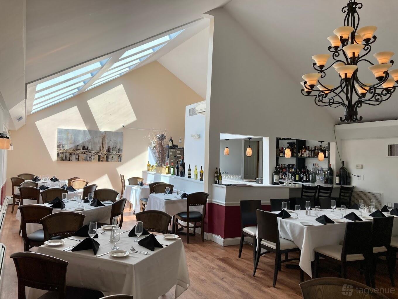 A restaurant dining room with skylights, white tablecloths, black napkins, and a bar area at Lenny's North Seafood & Steakhouse.