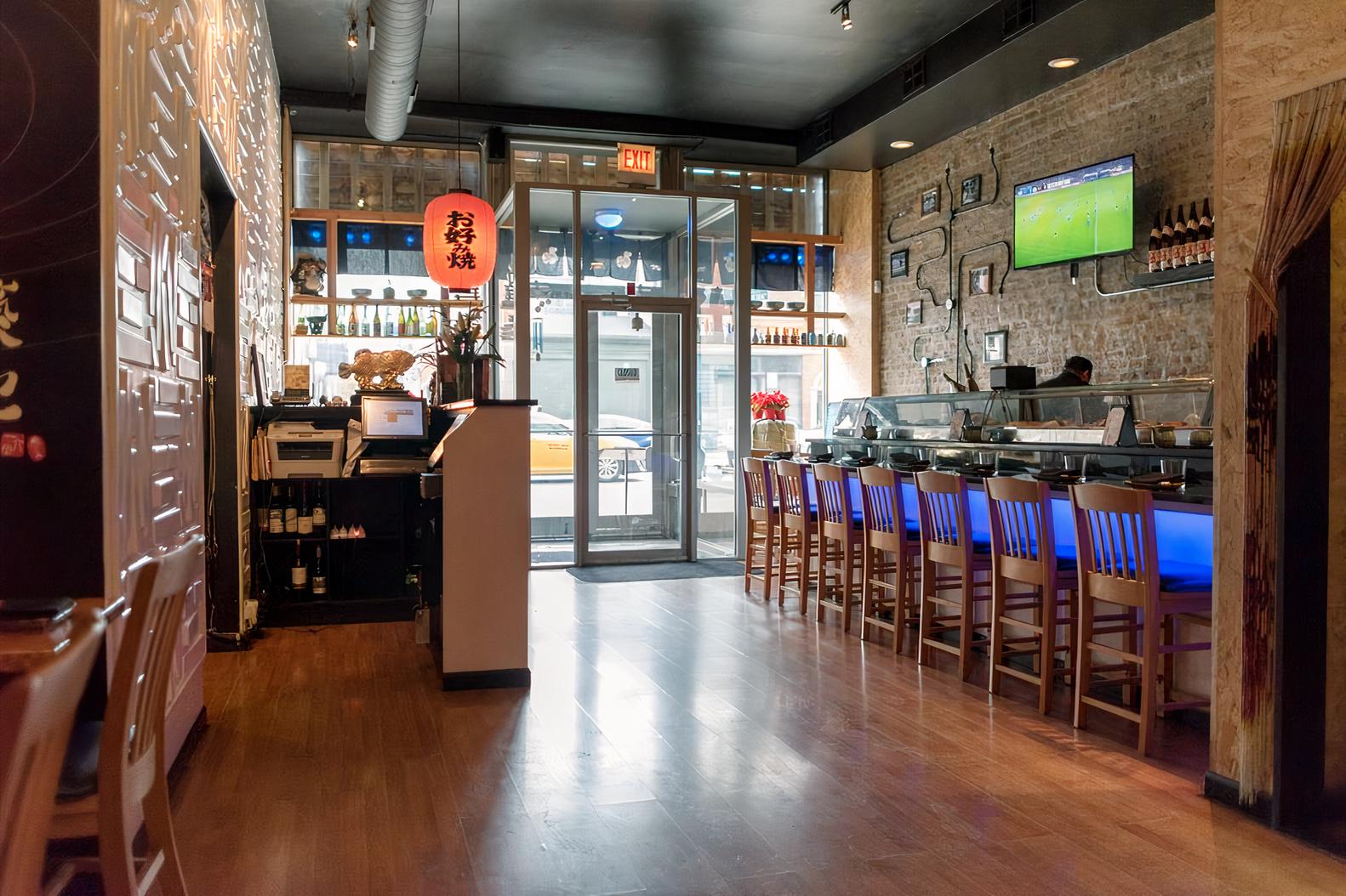 A restaurant with exposed brick walls, wooden floors, and a sushi bar with blue lighting at Tsukiji Sushi Sake Bar.