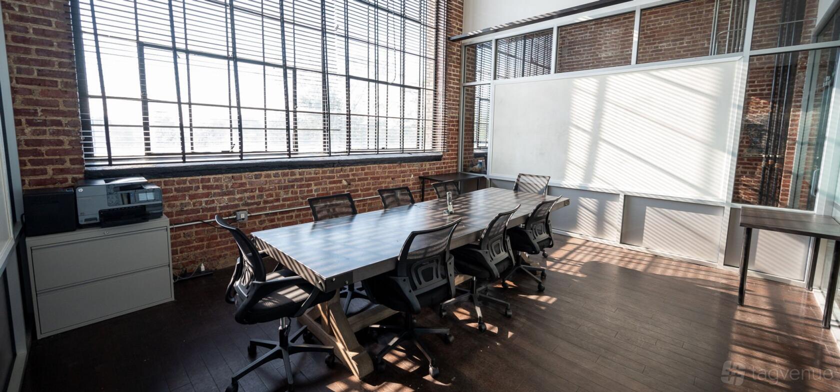 A conference room with exposed brick walls, large industrial windows, and a long meeting table at Crave Cave.