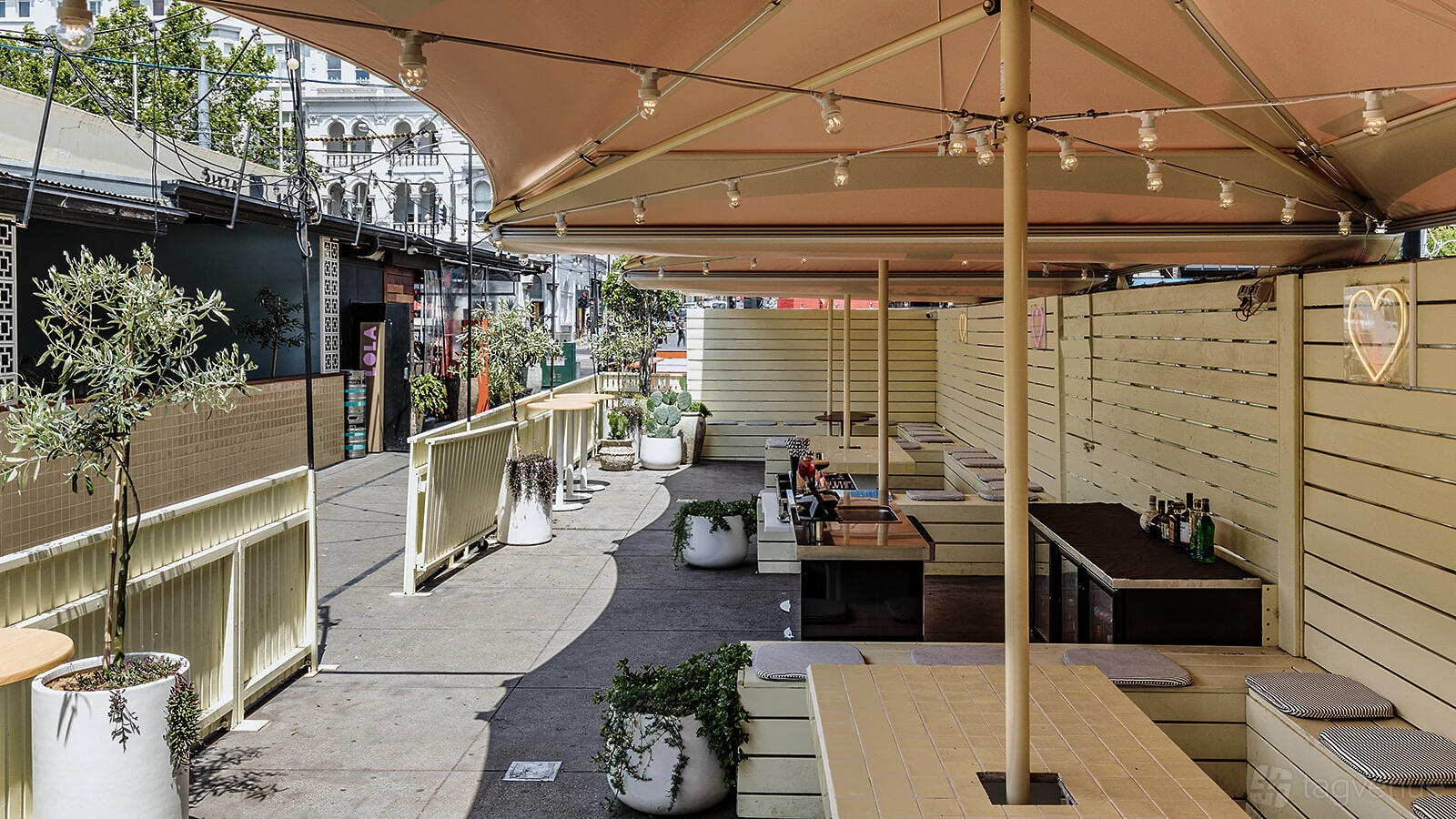 An outdoor terrace with large umbrellas, built-in benches, potted plants, and privacy screens at LOLA St Kilda.