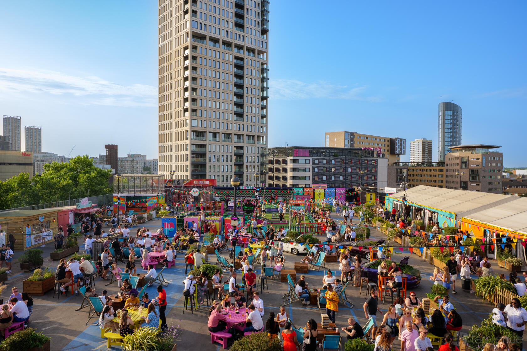 A rooftop venue with colorful seating, string lights, and people socializing at Roof East.