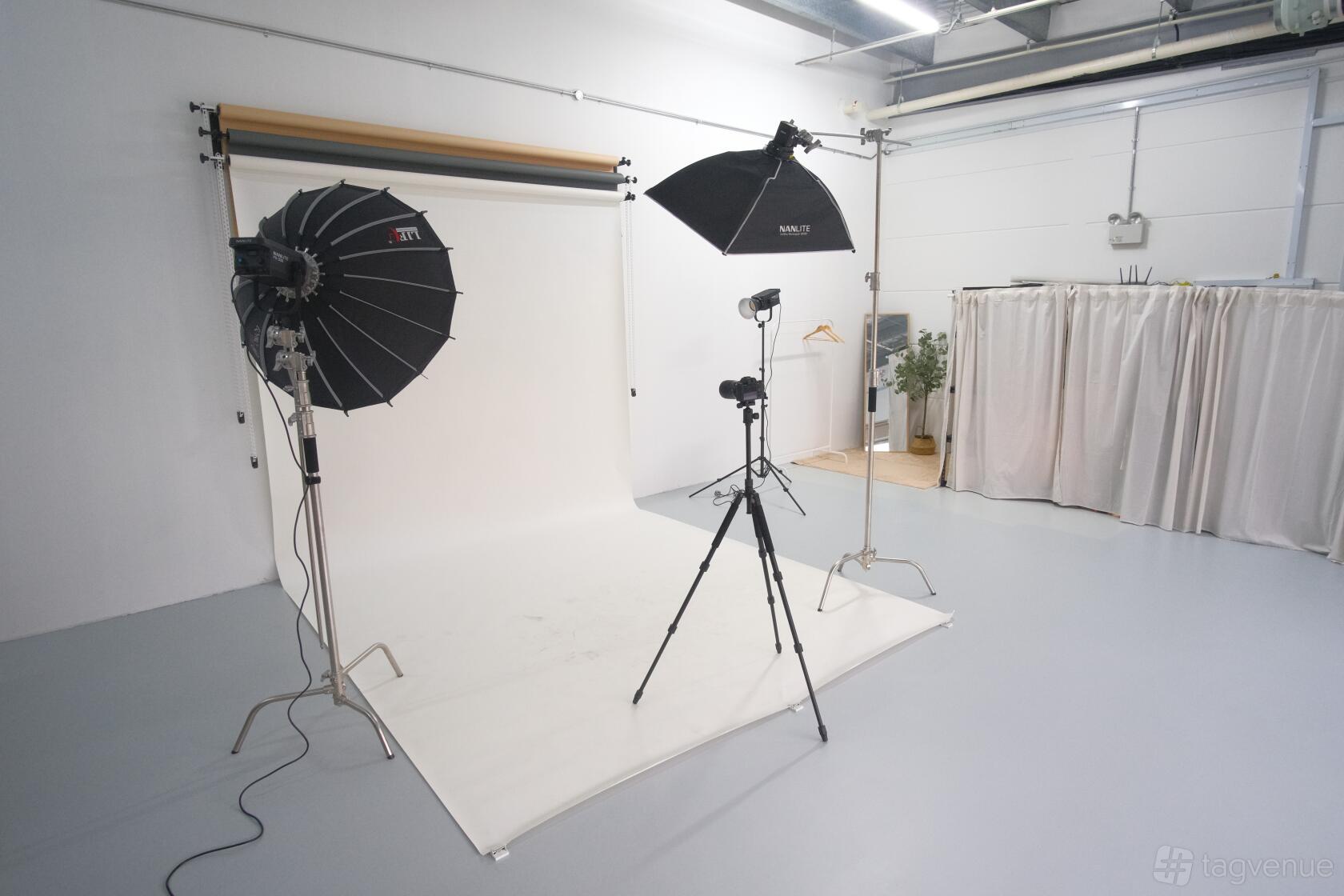 A photo studio with a white backdrop, studio lights, a camera on tripod, and curtained dressing area at Spaces Photo Studio.