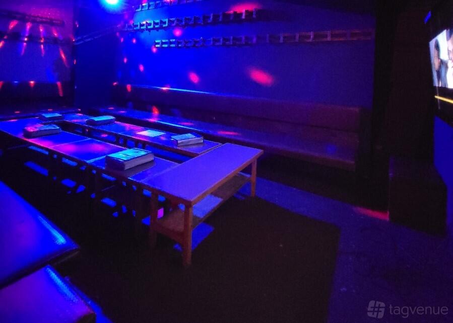 A private karaoke room with long bench seating, low tables, and colorful disco lighting at Beats Karaoke Cafe.