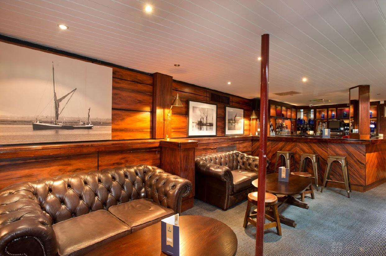 A lounge on a boat with tufted leather sofas, wood-paneled walls, and nautical artwork at The Tattershall Castle.