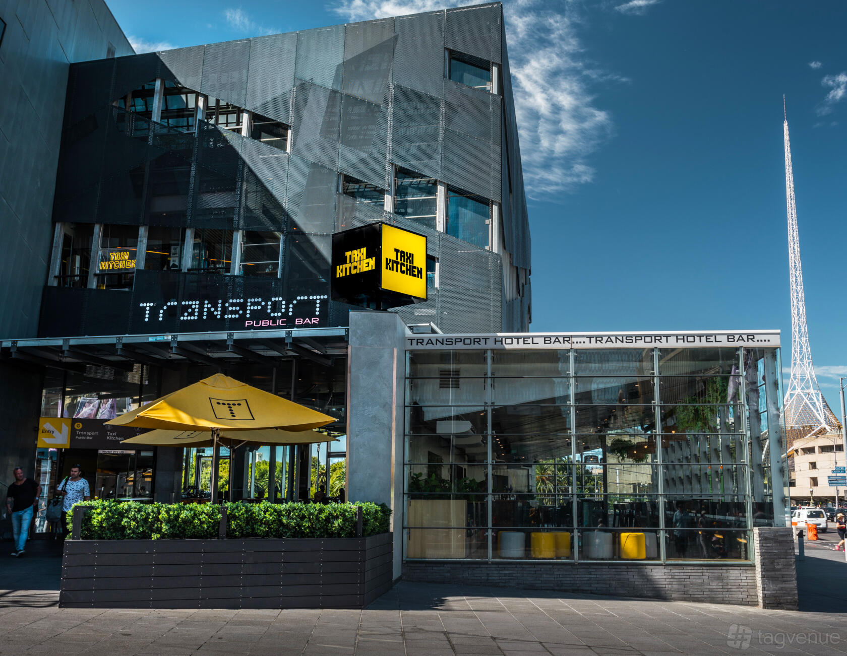 A pub with glass walls, outdoor seating under yellow umbrellas, and modern signage at Transport Public Bar.