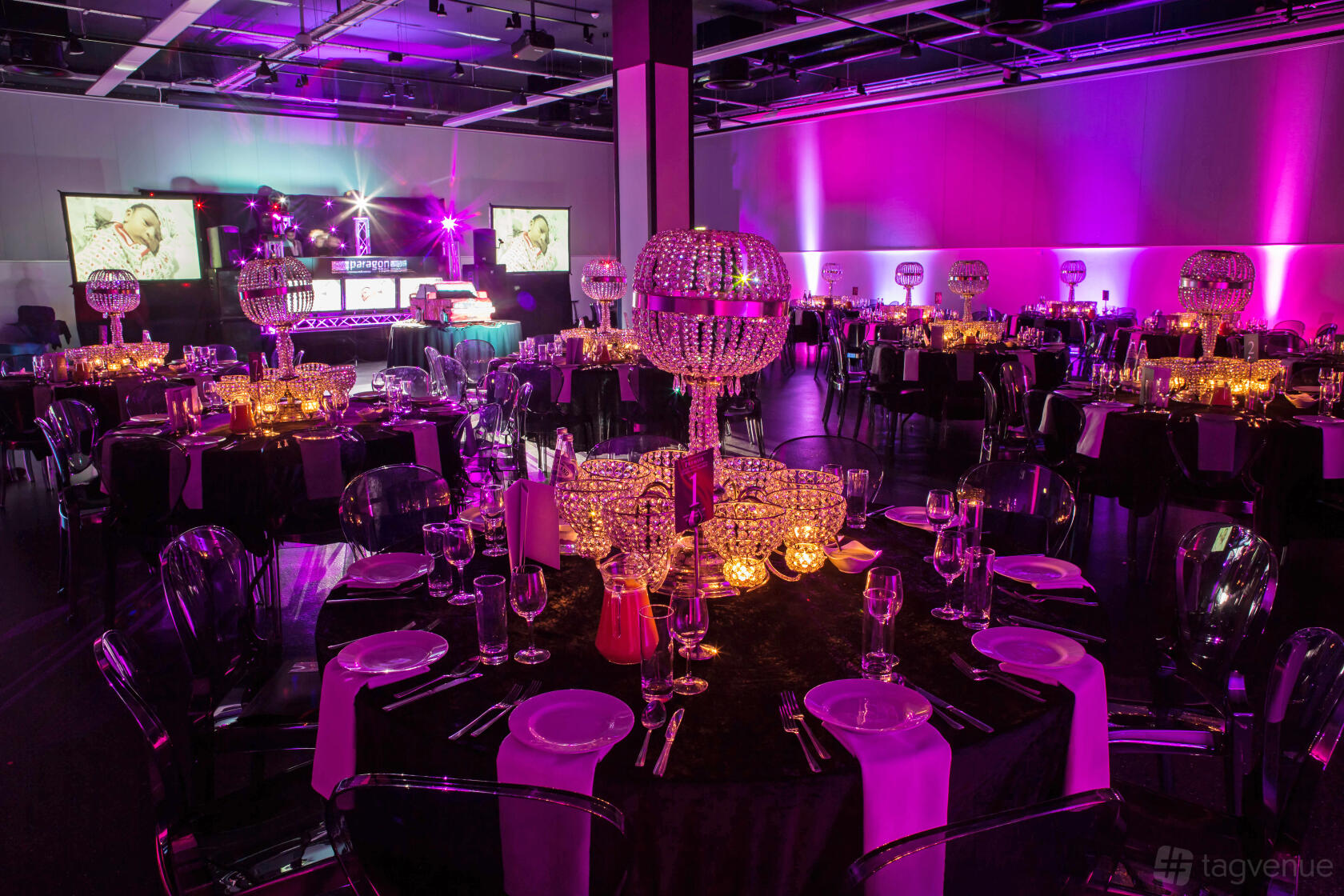 A conference hall with round tables set for dining, crystal centerpieces, and purple ambient lighting at Mercedes-Benz World.