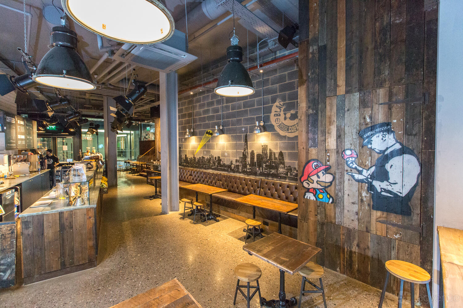 An event space in a cafe with exposed ductwork, industrial light fixtures, and mural art at Black Sheep Coffee Southbank Tower.