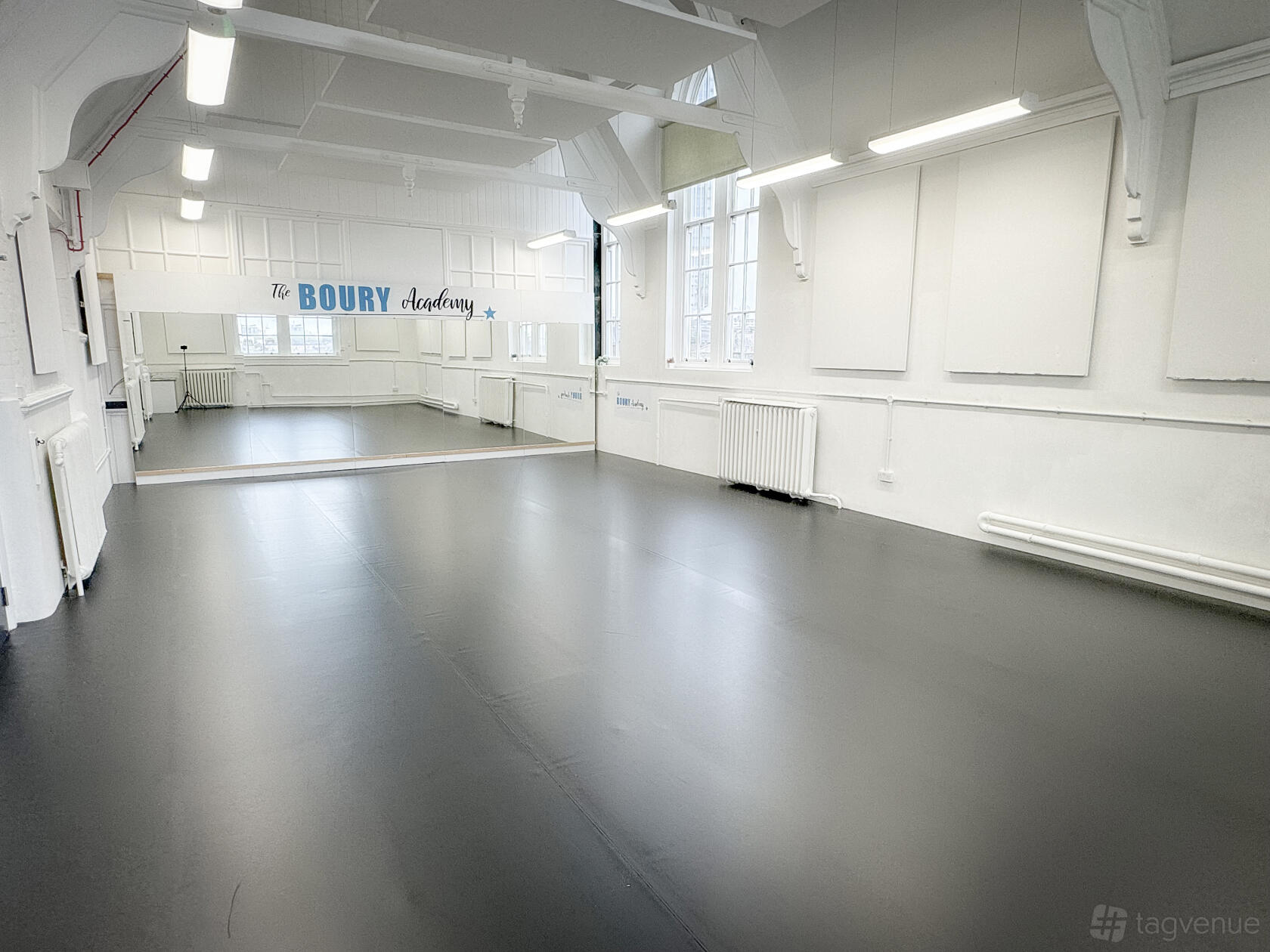 A rehearsal room with large mirrors, tall windows, and white walls at The Boury Studios.