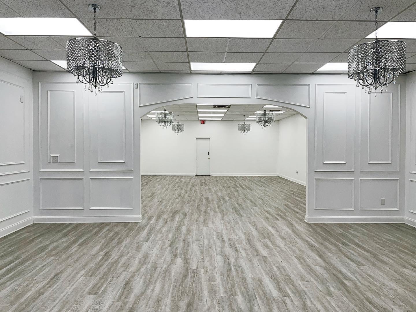 An event venue with light wood flooring, white paneled walls, and chandeliers at Mirrors Creative Studio.