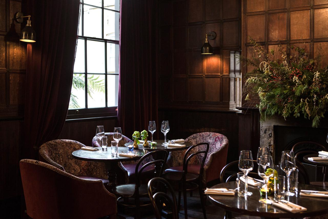 A function room with wood-paneled walls, large window, velvet curtains, and floral arrangements at The Cleveland Arms.
