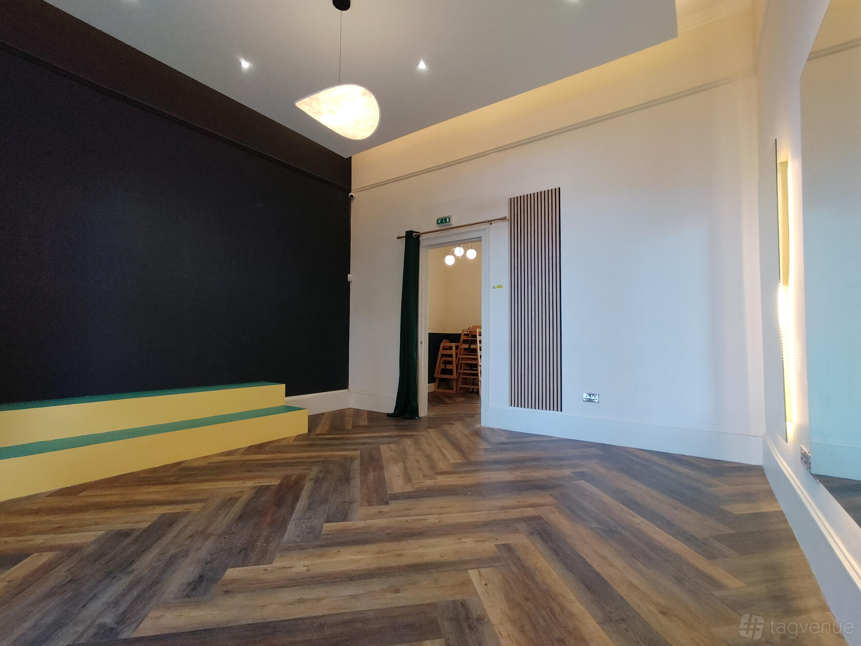 A photo studio with chevron wood flooring, a small yellow platform, and a matte black accent wall at Little Plaza.