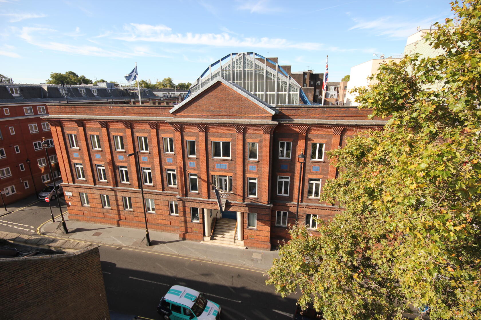 A red-brick versatile event space with tall windows, a glass rooftop structure, and flagpoles at London Scottish House.