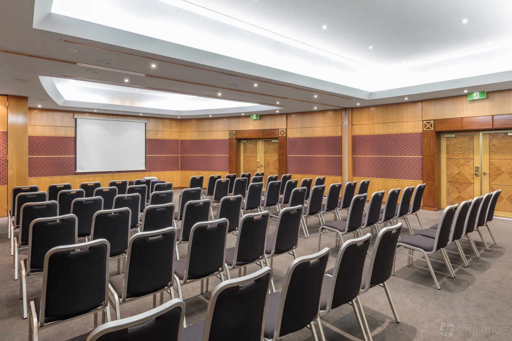 An event space in a hotel with theater-style seating, wood paneling, and a projector screen at View Sydney.