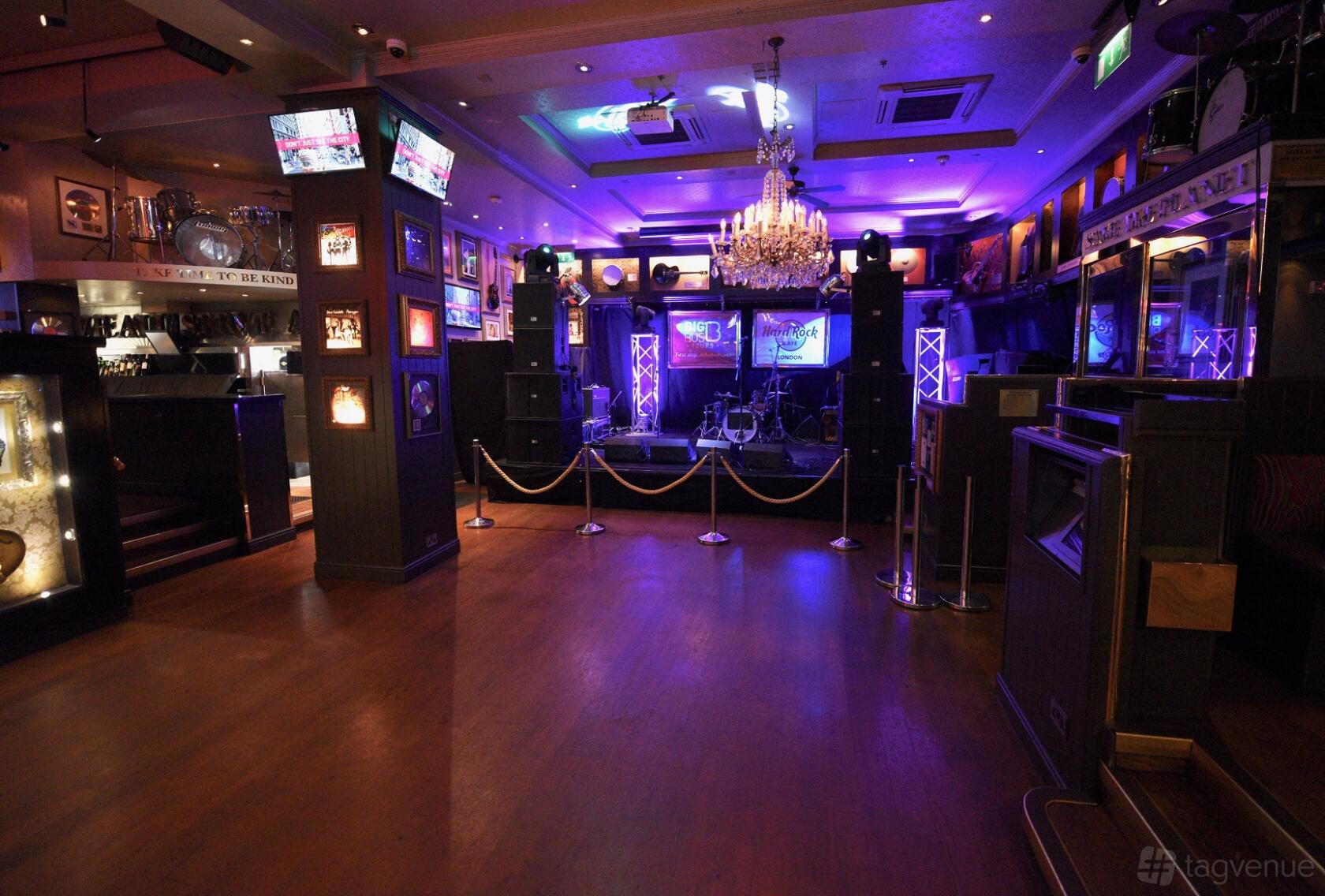 A cafe with a stage setup, purple lighting, chandeliers, and walls decorated with music memorabilia at Hard Rock Cafe London.