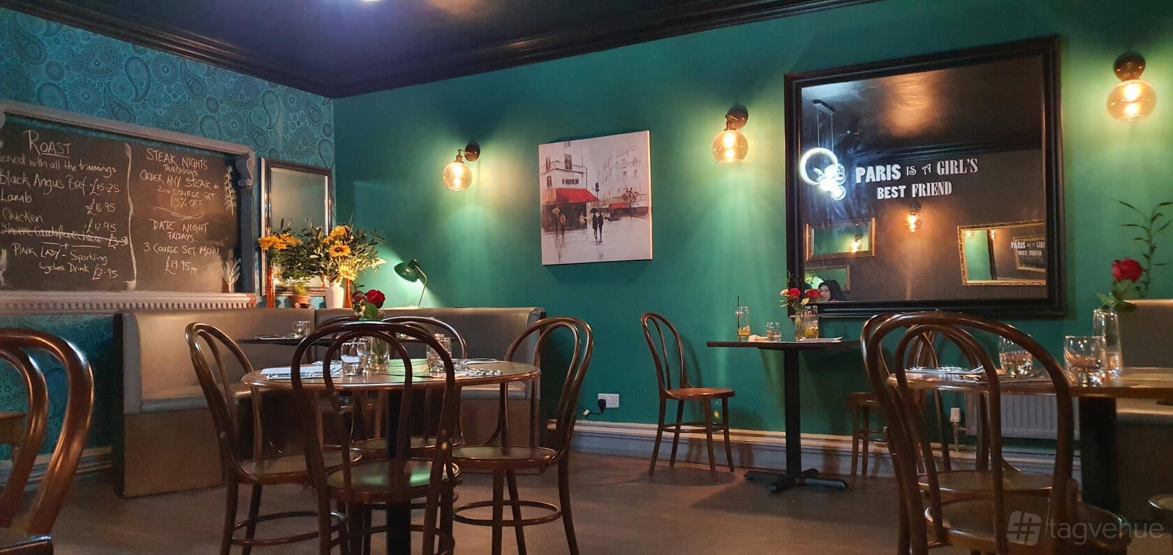 A restaurant with teal walls, wooden chairs, banquette seating, and wall-mounted lighting at Tarragon Bistro.
