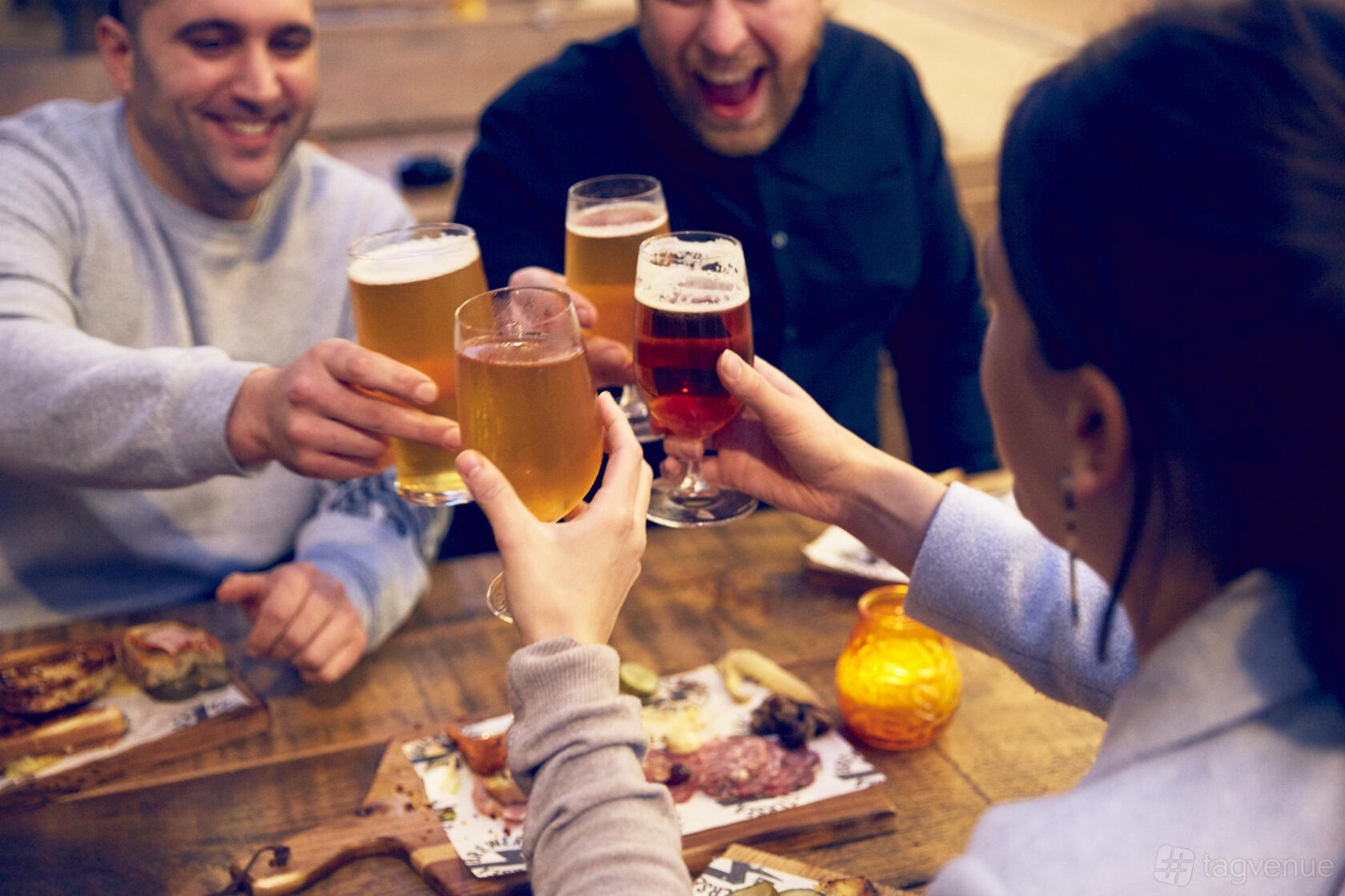 A pub with guests toasting glasses of beer over a wooden table with charcuterie boards at Battersea Brewery.
