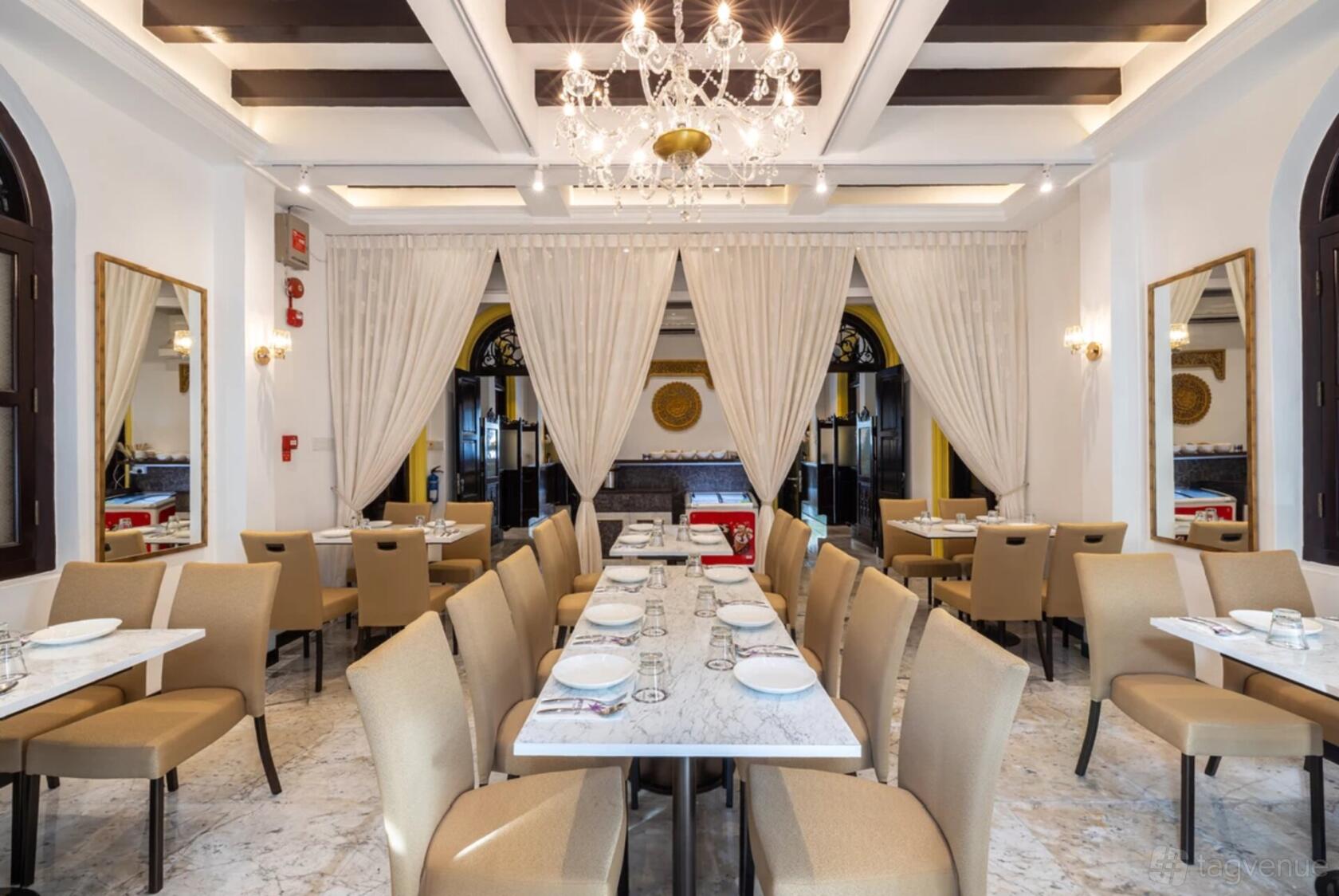 An event venue with chandeliers, marble flooring, beige upholstered chairs, and white draped curtains at Gedung Kuning.