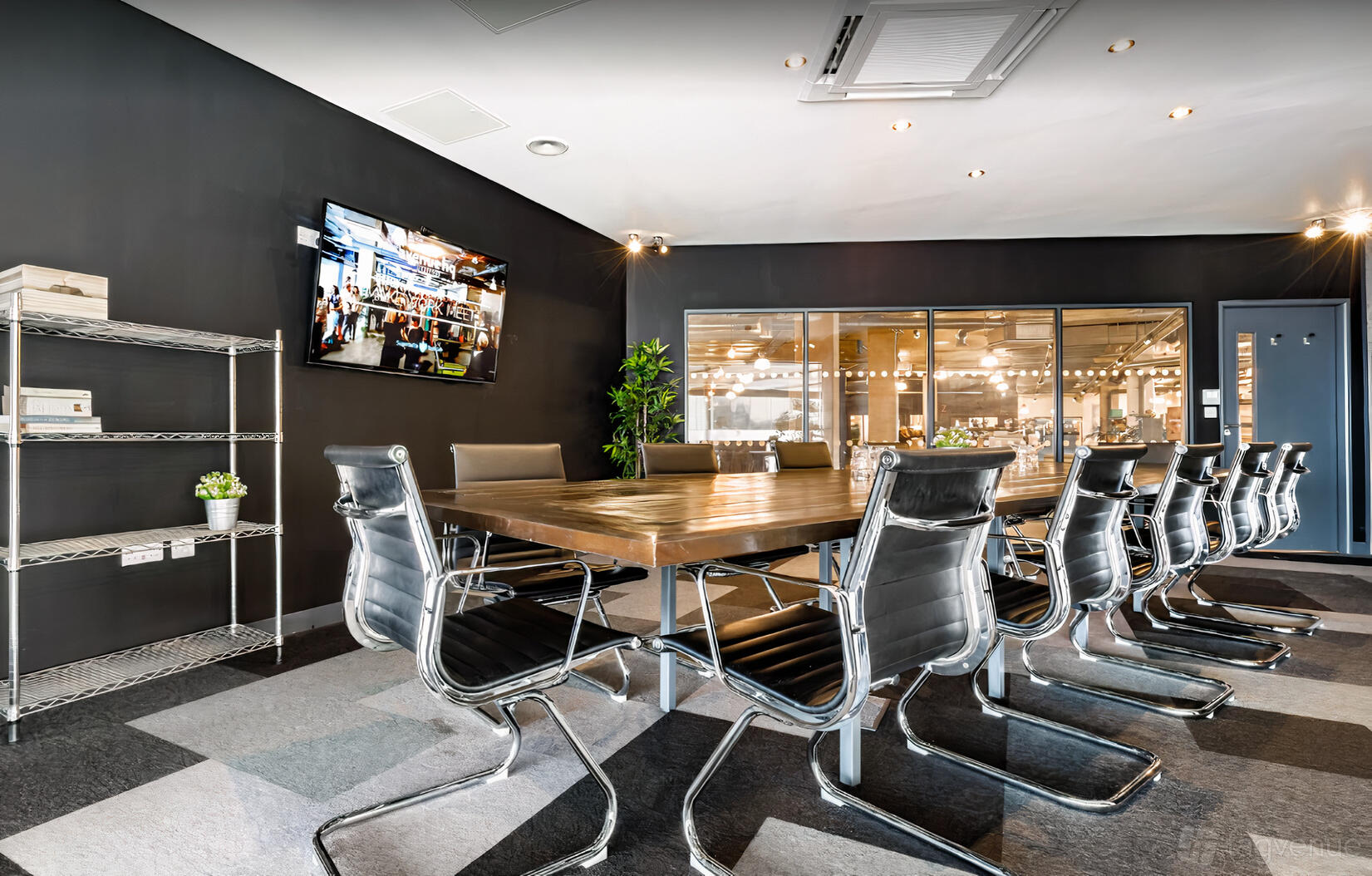 A boardroom with a large wooden conference table, leather chairs, wall-mounted TV, and glass partition at Avenue HQ Mann Island.
