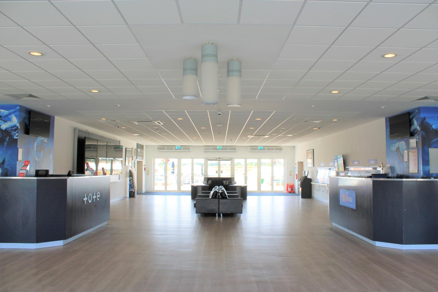 An event venue lobby with wood flooring, modern ceiling lights, and black leather seating at Chelmsford City Racecourse.