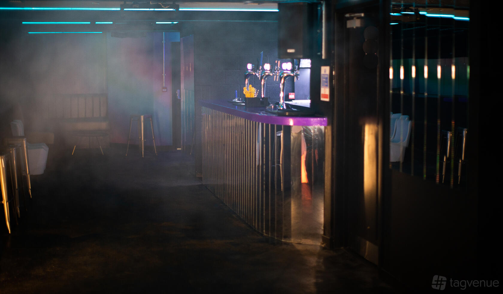 A nightclub basement with neon lighting, misty atmosphere, and a bar counter with beer taps at ZODIAC Karaoke Bar & Club.