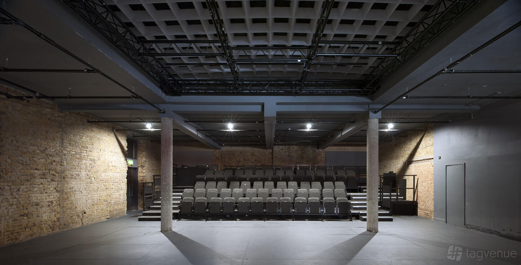 A theatre with exposed brick walls, tiered seating, and open ceilings with lighting rigs at Bush Theatre.