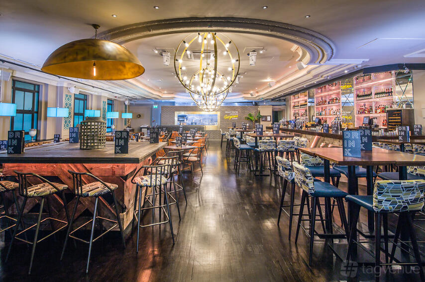 A bar with glowing pendant lights, patterned bar stools, and high tables at Sway.