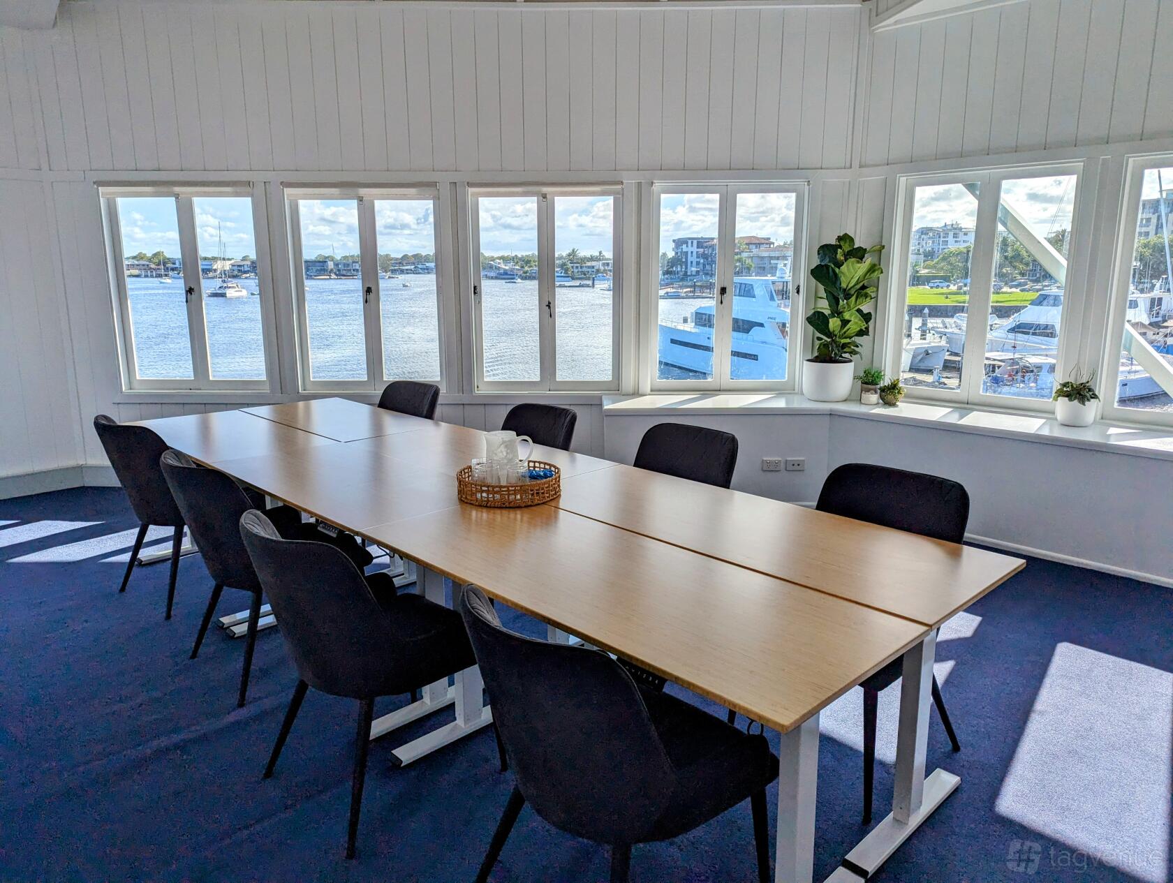 A boardroom with a long wood table, black chairs, and large windows overlooking a marina at Salty Spaces.
