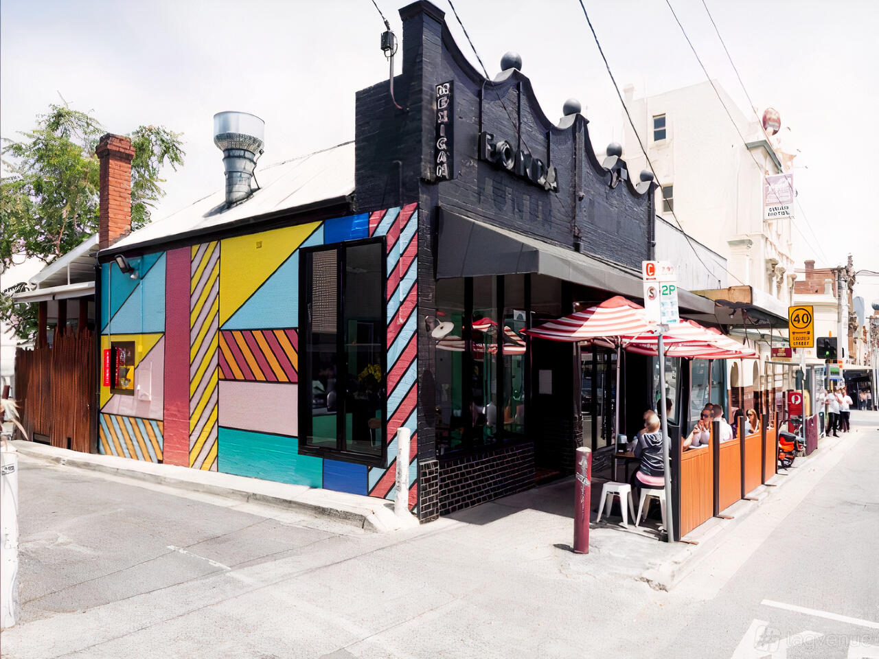 A restaurant with a colorful geometric mural exterior and outdoor seating with red-and-white umbrellas at Fonda Mexican @ Richmond.