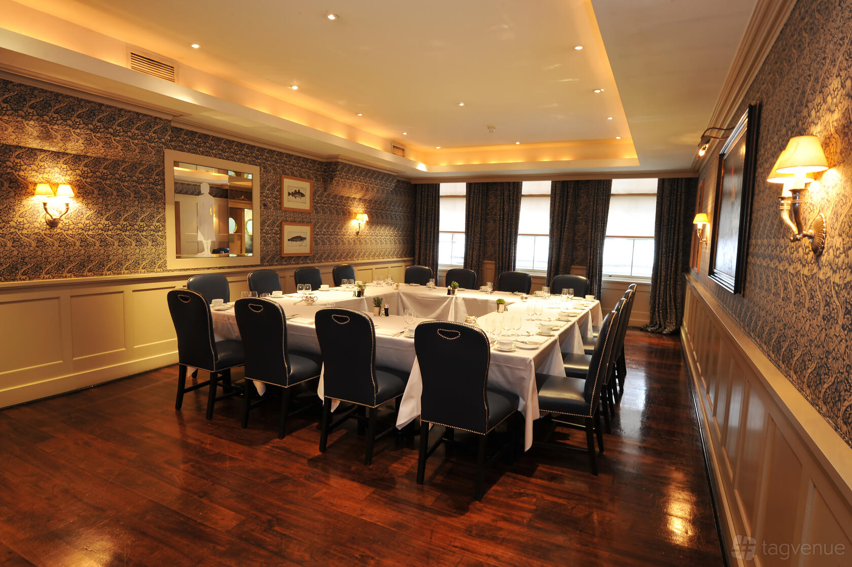 A dining room with patterned wallpaper, hardwood floors, and a U-shaped table with black chairs at Bentley's Oyster Bar & Grill.