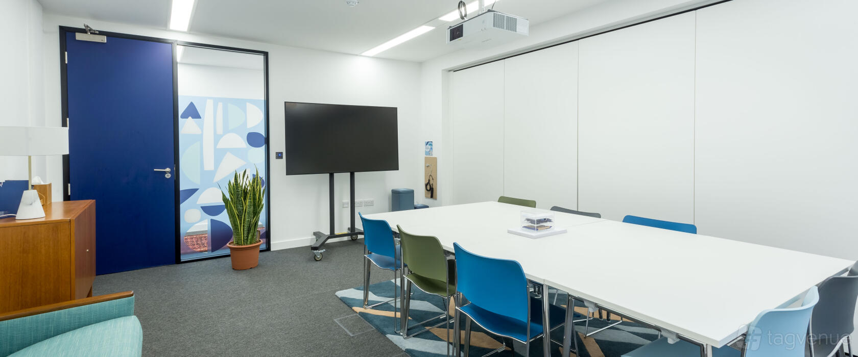 An event venue with a white conference table, colorful chairs, and a wall-mounted screen at Wallacespace Covent Garden - 53 Parker Street.