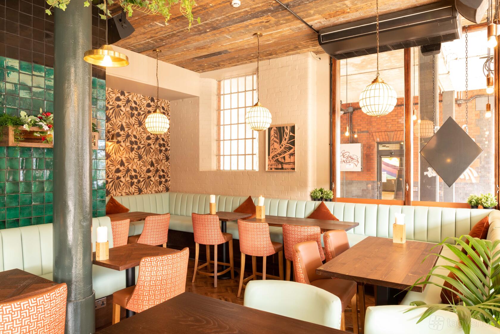 An event space in a pub with mint green booth seating, wooden tables, patterned accent wall, and large windows at The Bristol Stable.