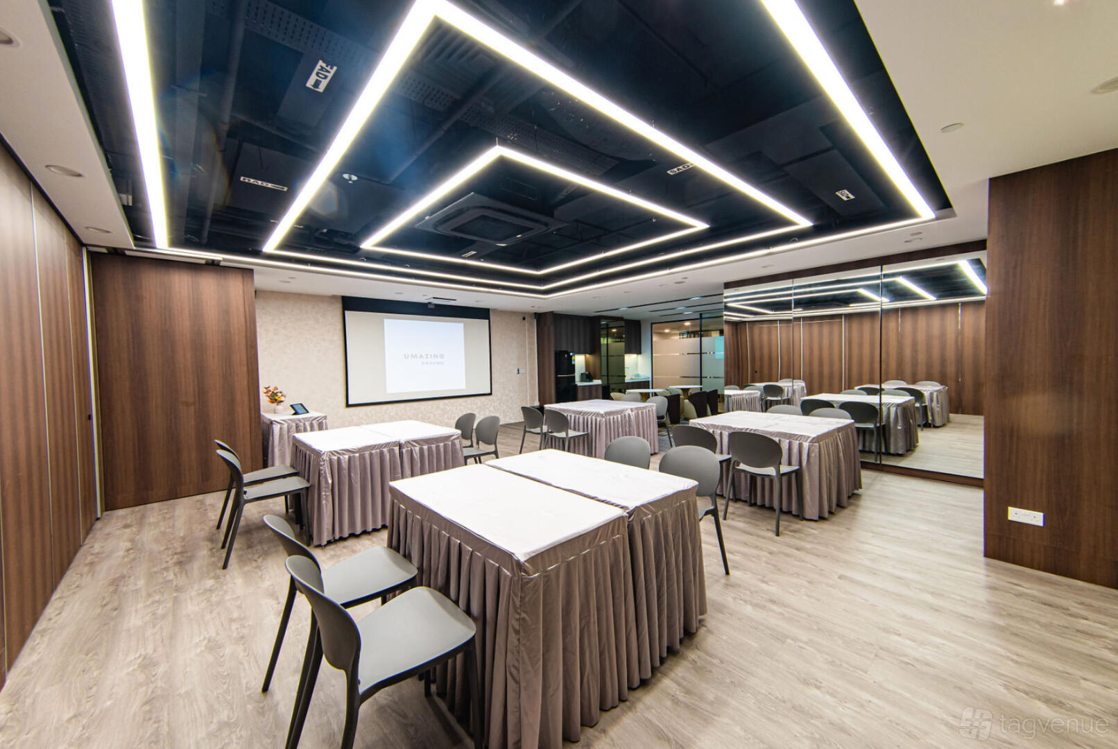 An event venue with wood-paneled walls, mirrored accents, and tables draped in gray linens at Umazing Events.