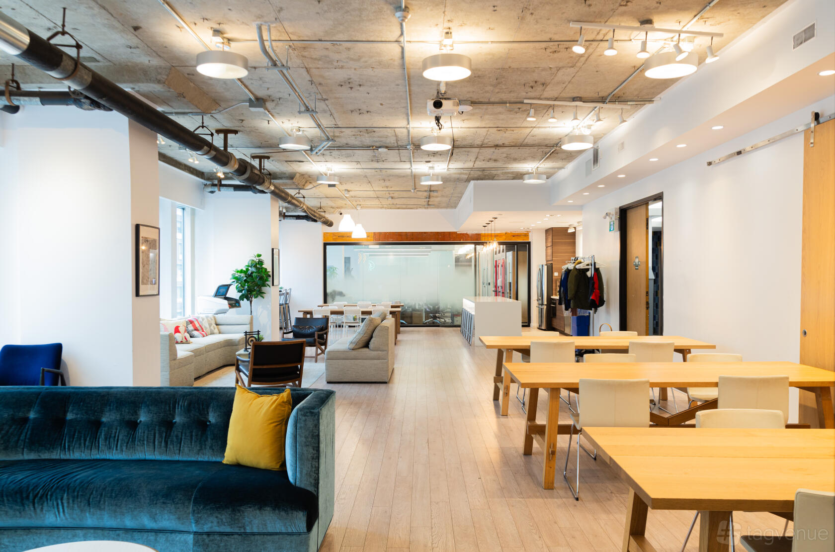 An open event area with exposed concrete ceiling, wooden floors, sofas, and wooden tables at Startuptive.