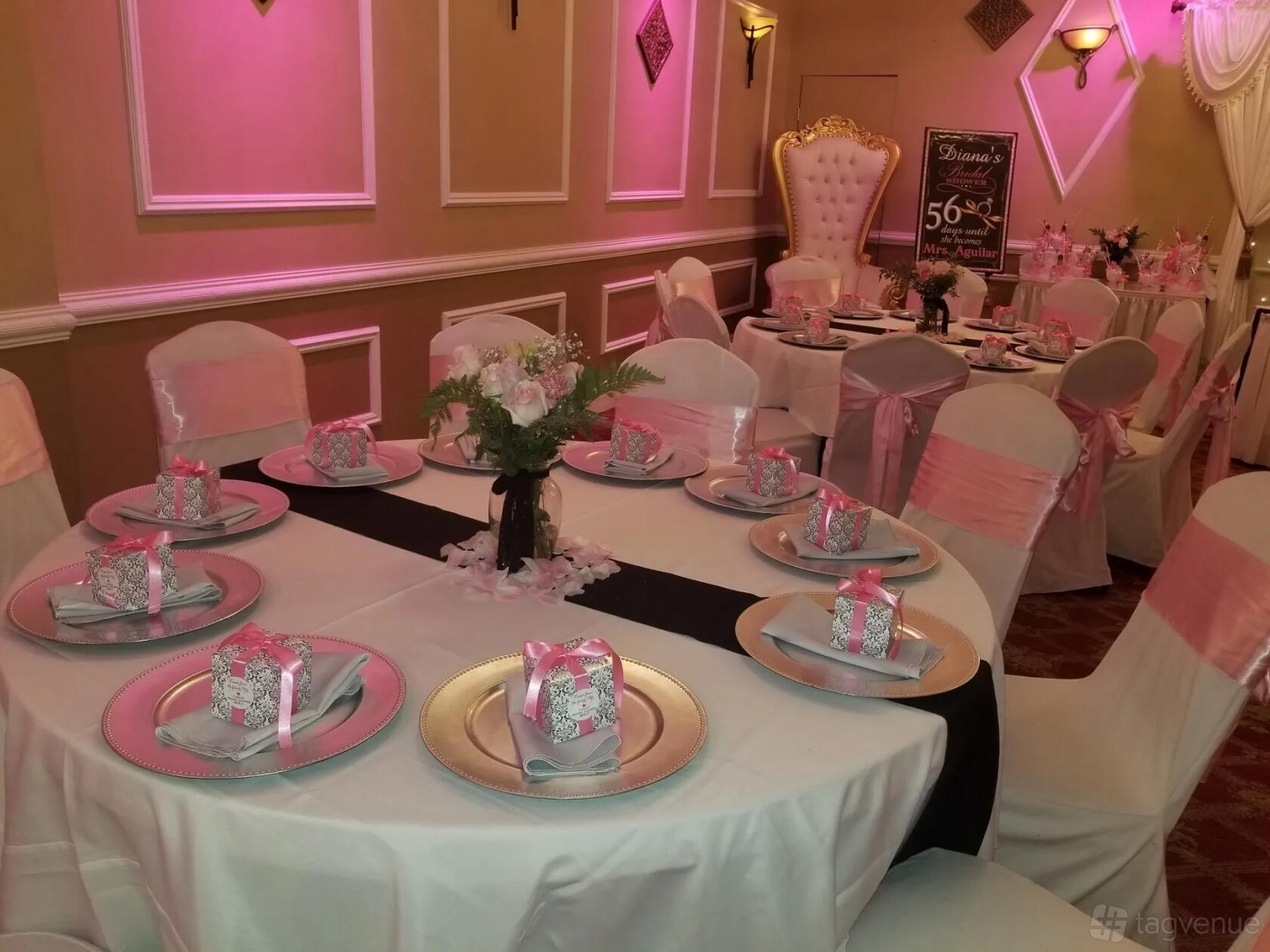 A banquet hall with round tables dressed in white linens, pink chair sashes, and gift boxes at The Grand 2020 Banquet & Party Hall.