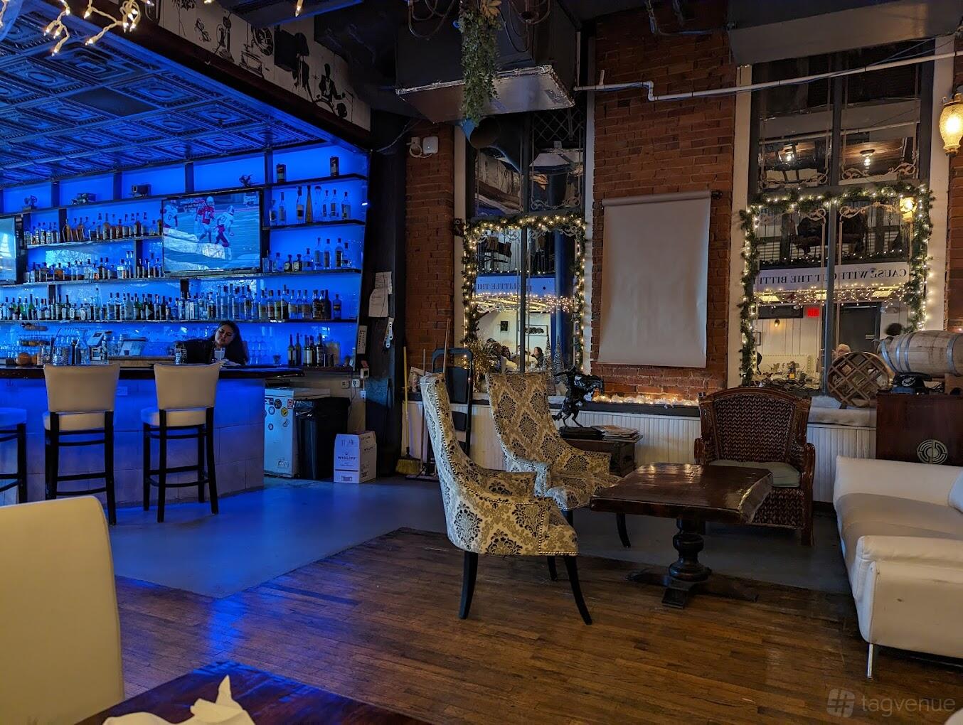 An event space in a restaurant with a blue-lit bar, upholstered chairs, exposed brick, and large windows at 3Eleven Kitchen and Cocktails.