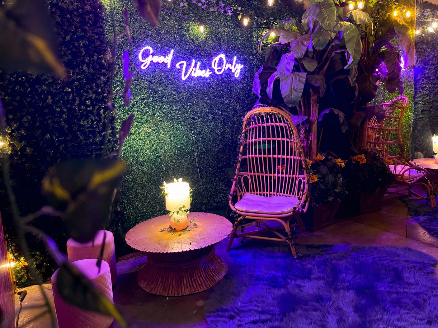 A photo studio with faux greenery walls, rattan chairs, purple neon sign, and string lights at Jungle House Studios.