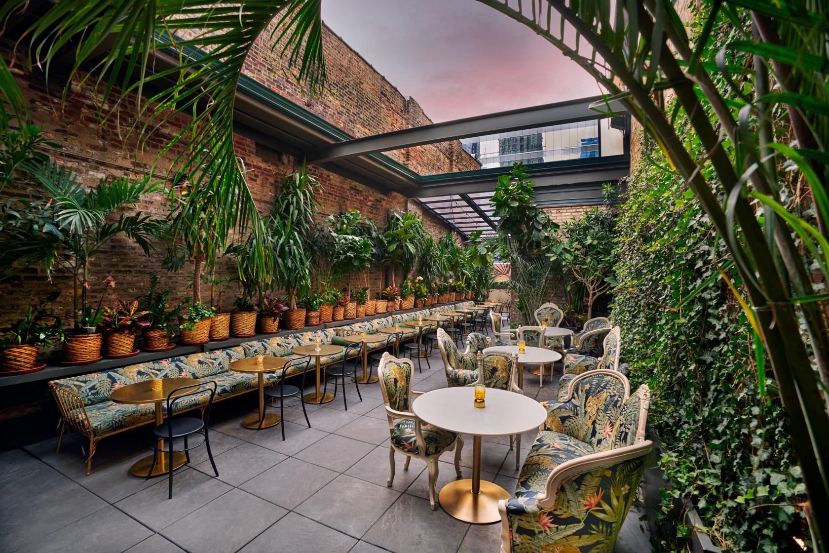 An outdoor cocktail bar with tropical plants, patterned armchairs, and round tables at Celeste Garden.