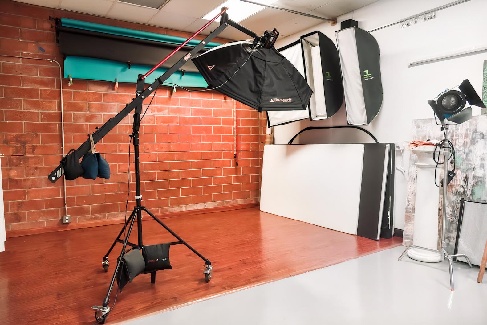 A photo studio with a brick accent wall, studio lighting equipment, and colored backdrop rolls at Noho Photo Studio.