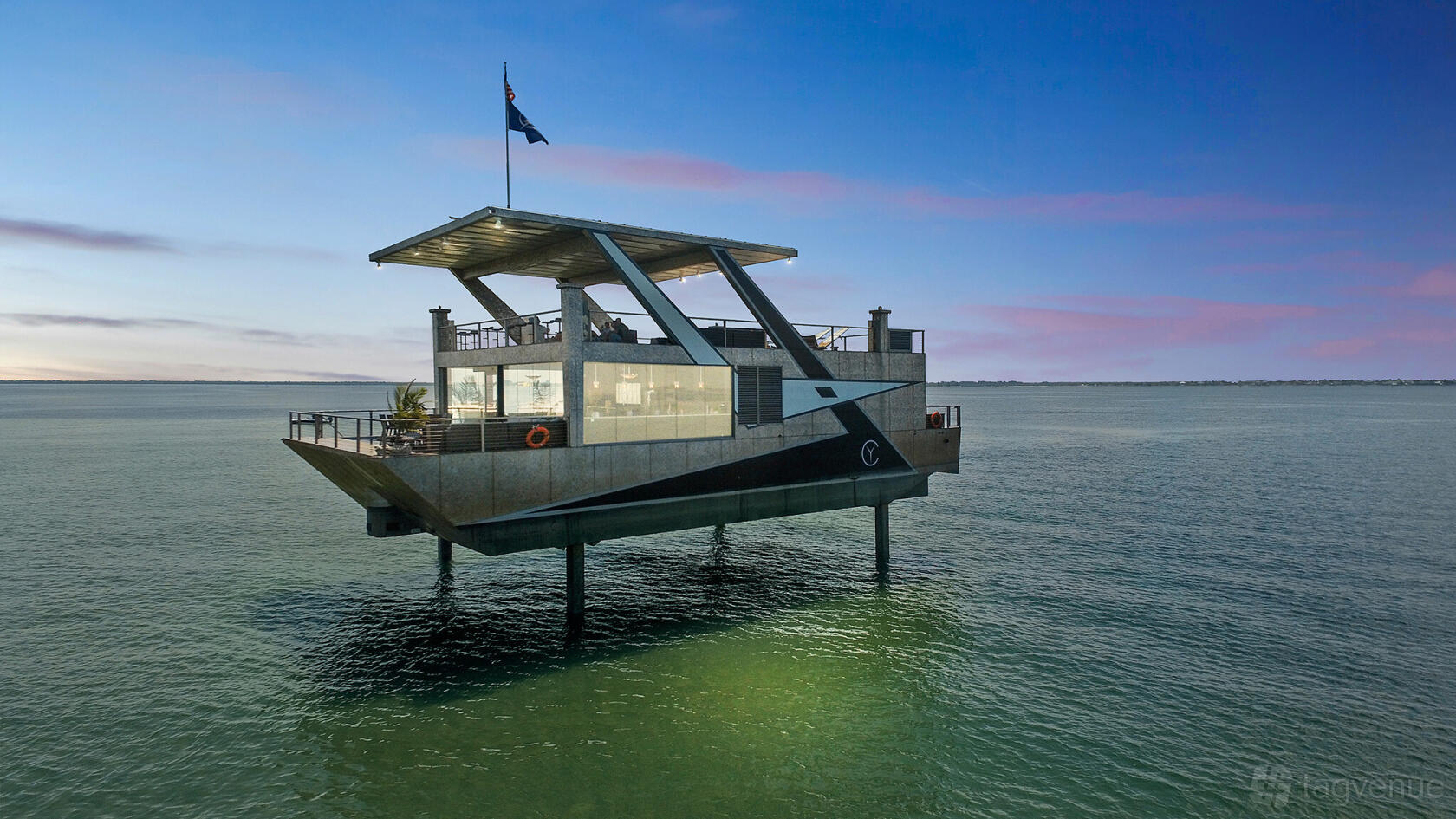 A modern houseboat with expansive windows and an open upper deck on the water at Mansion Yachts.
