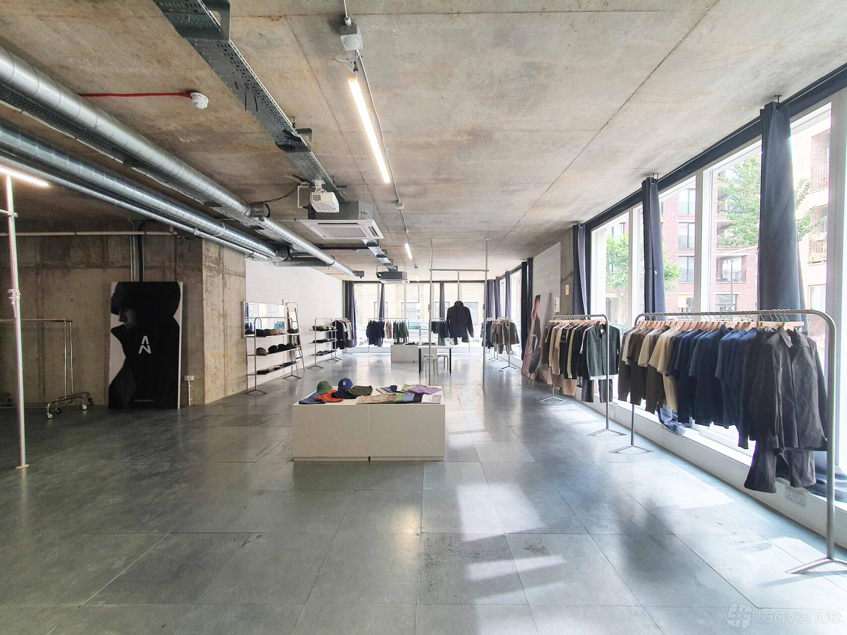 An event space with floor-to-ceiling windows, exposed ductwork, and clothing racks at Indra Gallery.