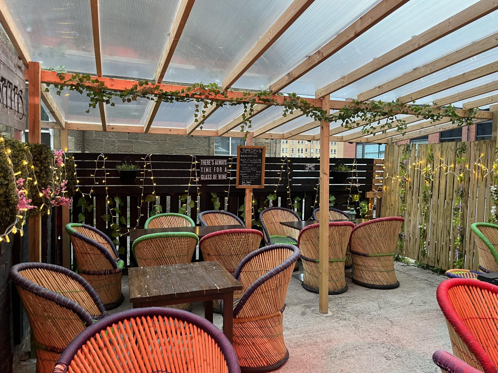 A terrace bar with multicolored wicker chairs, string lights, and a clear roof at 91B Private Venue.