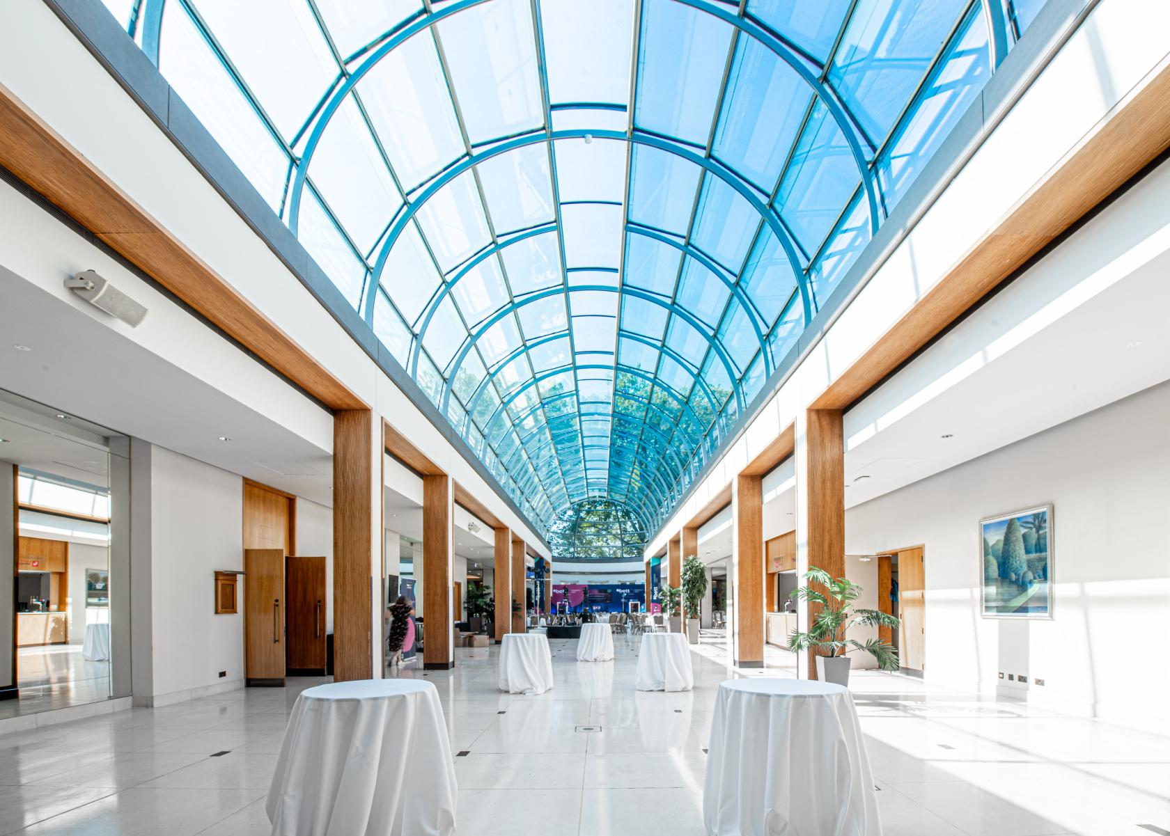 An event venue with a glass arched ceiling, marble floors, and cocktail tables at The Hurlingham Club.