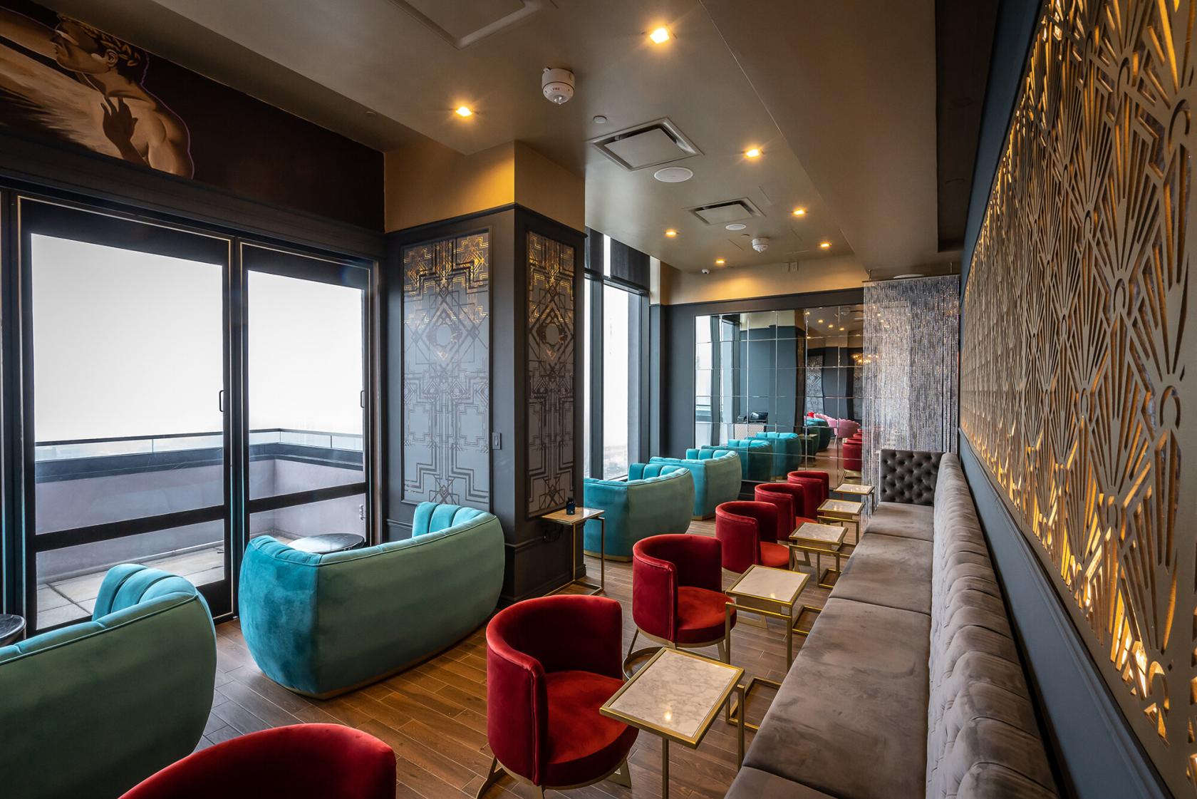 A cocktail bar with velvet lounge seating, gold-patterned walls, and marble-topped tables at Dear Irving on Hudson Rooftop.