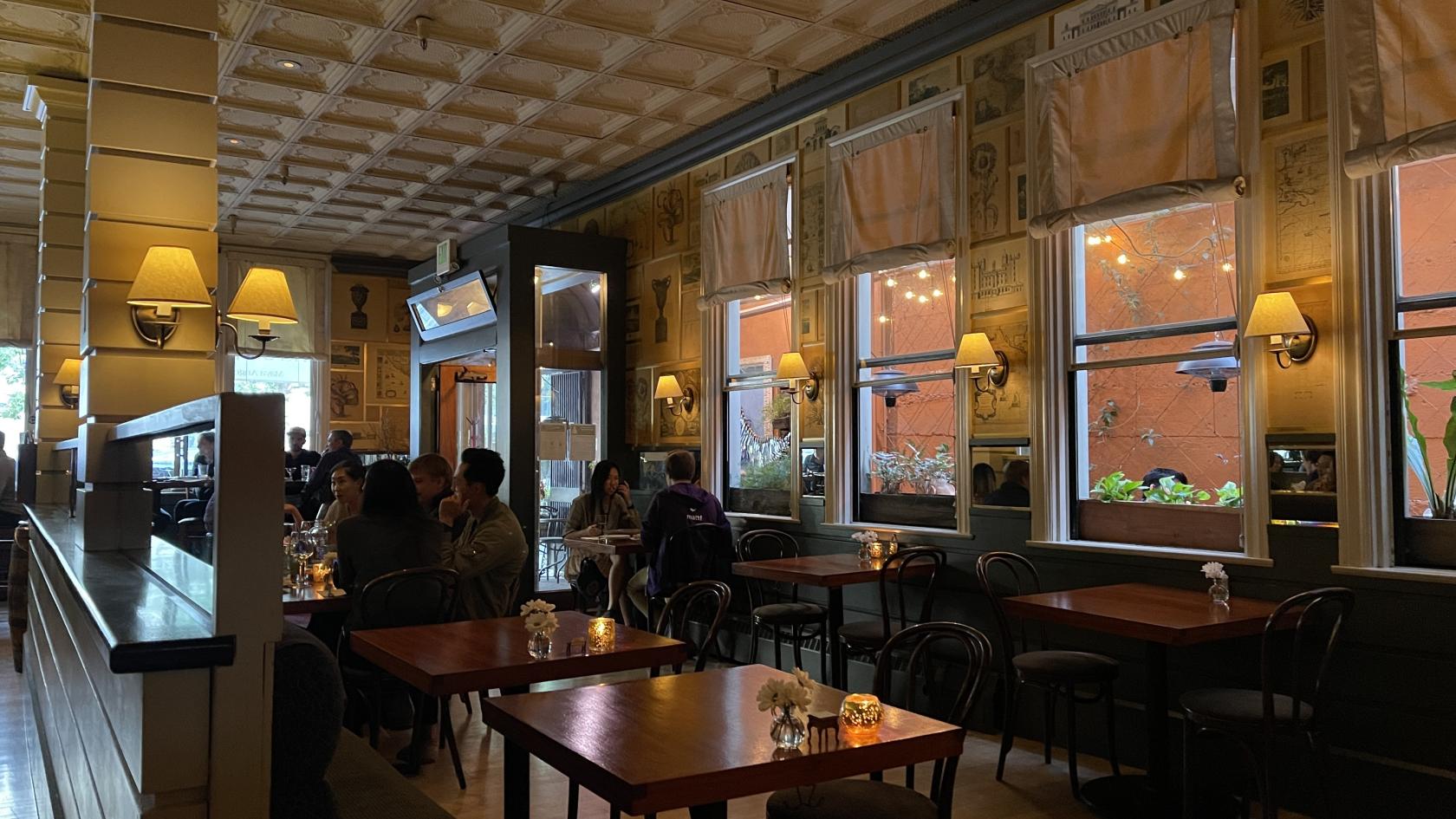 A restaurant dining room with wooden tables, wall sconces, and large windows at The Fly Trap.