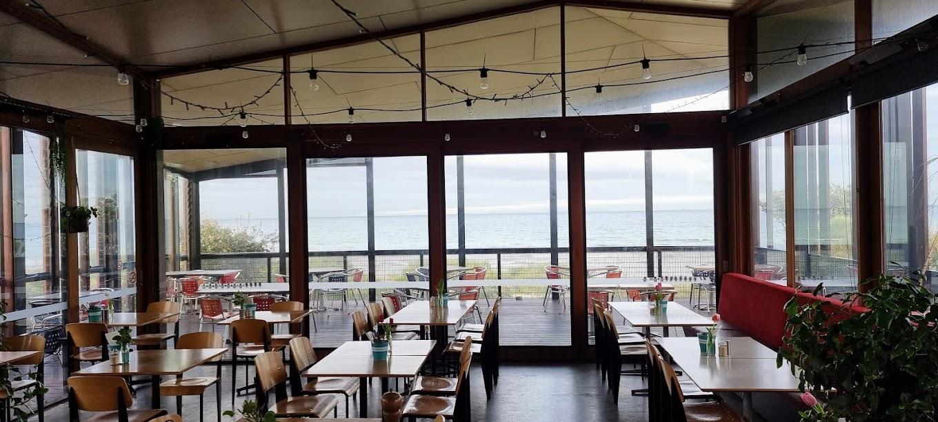 A function room with floor-to-ceiling windows, ocean views, and wooden tables set for dining at Crackerjack Beachfront.