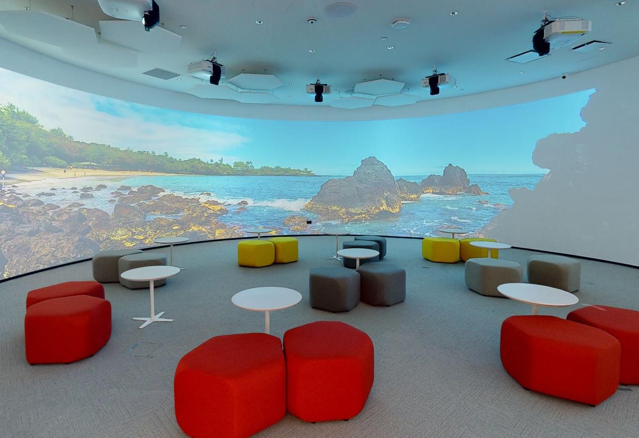 An auditorium with tiered, colorful ottomans and large curved digital wall projection at Catapult.
